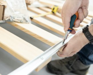 Close up of hands assembling a split box spring with a screwdriver.