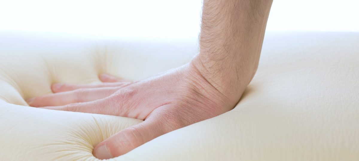 Hand is pressing a memory foam mattress. Learn all about foam mattresses.