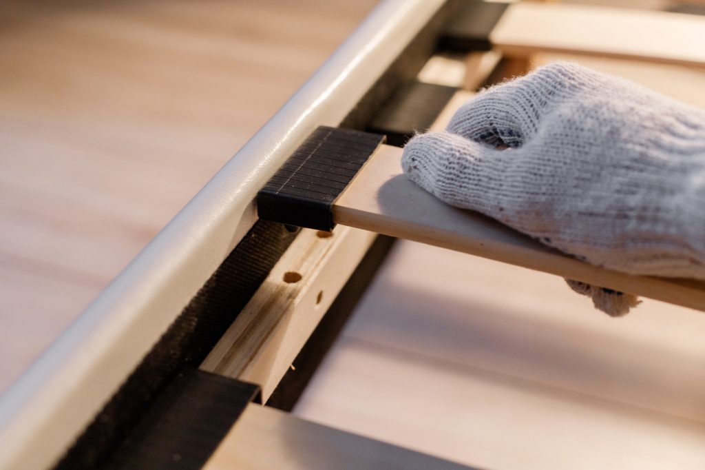 Frames Or Boxsprings? Male worker's hand in glove assembling bed, connecting slats to bed frame.