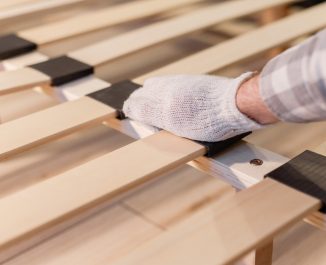 Male worker's hand in glove assembling bed, connecting slats to bed frame. Frames or boxsprings?