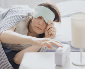 Woman in bed with a sleep mask wakes up and turns off the alarm. a clock with a timer, a woman yawns.